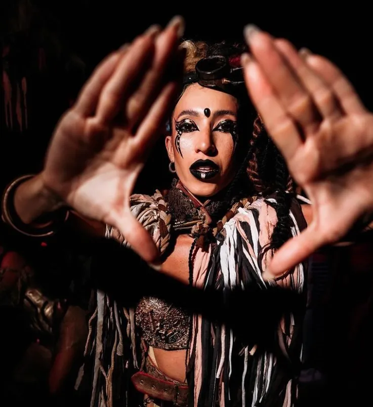 Performer con maquillaje tribal enmarcando la cámara con las manos